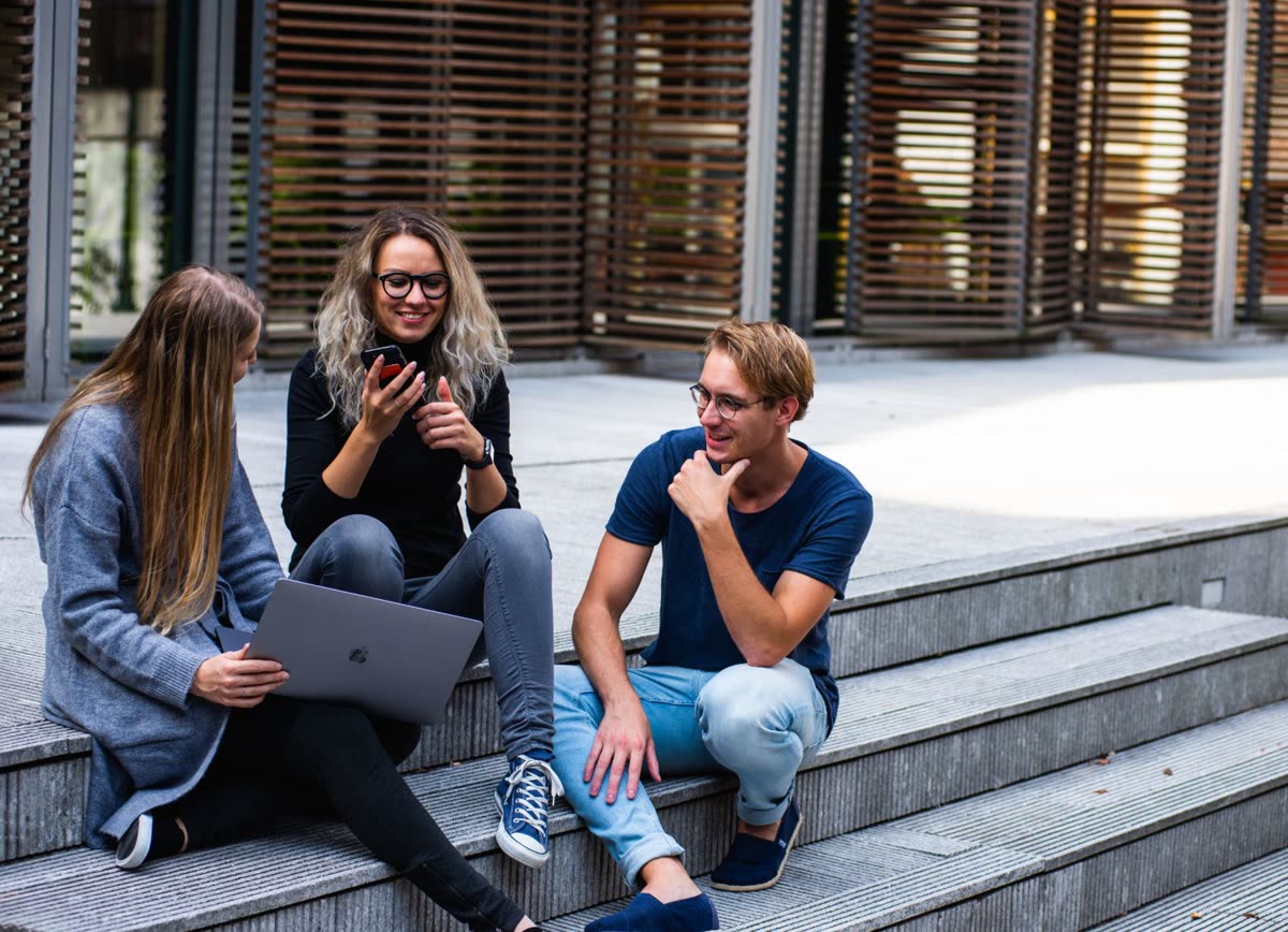 Three marketers talking on outdoor steps, one with a laptop and one with a phone